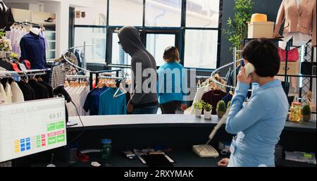 Rapinatore afroamericano che ruba camicia di base in una boutique moderna, essendo catturato dalla guardia di sicurezza asiatica. Ladro che corre dalla guardia del corpo, cercando di sfuggire alle accuse. Concetto di crimine Foto Stock