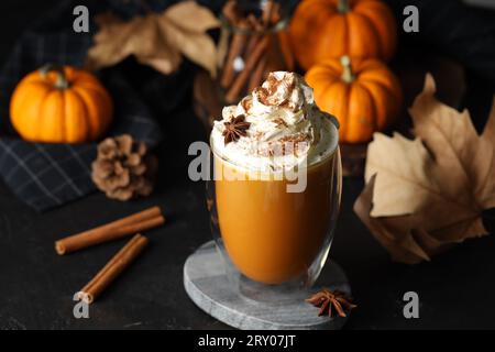 Bicchiere di latte di zucca con panna montata e ingredienti su tavola nera Foto Stock