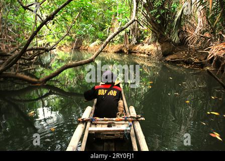 Un ranger del parco nazionale che indossa una giacca Brimob (Indonesian Mobile Brigade Corps) viene fotografato mentre pesca da una barca sul fiume Cigenter, mentre si ferma per viaggiare attraverso la foresta costiera dell'isola di Handeuleum nel parco nazionale di Ujung Kulon, Pandeglang, Banten, Indonesia. Un parco nazionale ben gestito ha una strategia competente e appropriata per prevenire la perdita di biodiversità e il cambiamento climatico, e migliorare la società locale mantenendo nel contempo il funzionamento essenziale degli ecosistemi, da cui dipende l'umanità in tutto il mondo, secondo gli scienziati. Tuttavia, grandi aree dei parchi nazionali sono state... Foto Stock