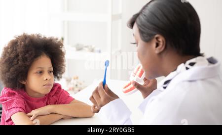 Dentista afroamericano che spiega ai bambini afro di razza mista come lavarsi i denti. Il concetto medico e sanitario per i bambini. Foto Stock