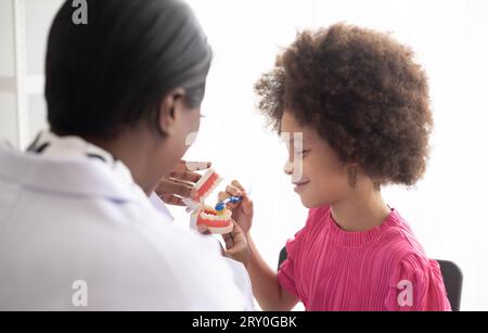 Dentista afroamericano che spiega ai bambini afro di razza mista come lavarsi i denti. Il concetto medico e sanitario per i bambini. Foto Stock