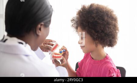 Dentista afroamericano che spiega ai bambini afro di razza mista come lavarsi i denti. Il concetto medico e sanitario per i bambini. Foto Stock