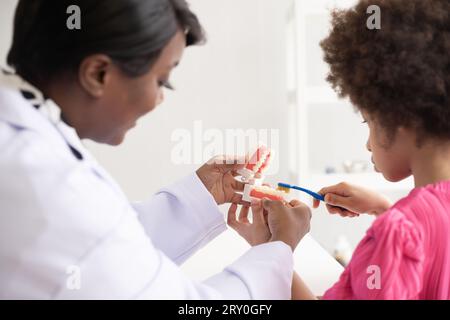 Dentista afroamericano che spiega ai bambini afro di razza mista come lavarsi i denti. Il concetto medico e sanitario per i bambini. Foto Stock