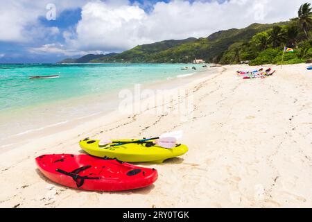 Vista sulla spiaggia delle Seychelles. Kayak di plastica colorati si stagliano sulla sabbia bianca in una giornata di sole Foto Stock