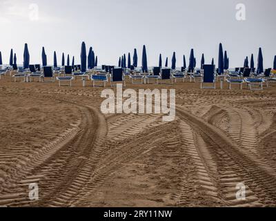 Lettini e ombrelloni bagnati sulla spiaggia di mare durante le giornate piovose. Ombrellone arrotolato sulla spiaggia contro nuvoloso scuro Foto Stock