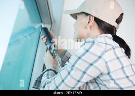 donna concentrata che applica silicone alla finestra Foto Stock