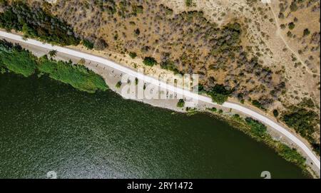 Vista aerea del sentiero bianco del parco tra una collina con cespugli e un lago verde. Tbilisi, Georgia. Lago Lisi. Foto di alta qualità Foto Stock