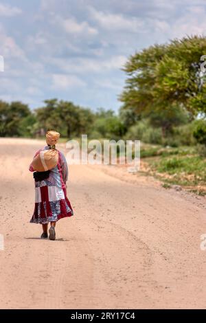 donna africana basarwa che cammina su una strada sterrata nel villaggio tradizionale Foto Stock