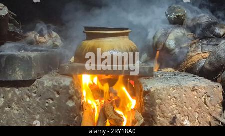 un bollitore marrone con cibo cotto e affumicato sotto il fuoco in una vecchia stufa tradizionale che brucia con legna da ardere Foto Stock