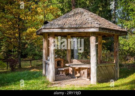 Gazebo in legno e stufa a mattoni per cucinare cibo all'aperto. Parco pubblico con tavolo da picnic e panca Foto Stock