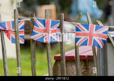 Union Jack che si accosta su una recinzione, molte bandiere in fila su una corda, davanti alle decorazioni del giardino ve day nel Regno Unito, Foto Stock