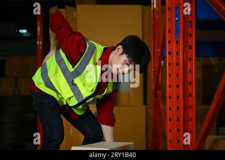 Turbato lavoratore maschile che soffre di mal di schiena mentre cerca di trasportare una scatola pesante. Concetto di lavoratori industriali e industriali Foto Stock