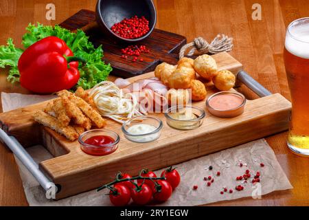 Ampia scelta di spuntini per la birra: Palle di formaggio fritte, formaggio a coda di cavallo, prosciutto e bastoncini di granchio serviti con salse all'aglio, ketchup e senape su un woo Foto Stock