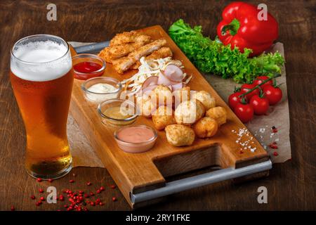 Ampia scelta di spuntini per la birra: Palle di formaggio fritte, formaggio a coda di cavallo, prosciutto e bastoncini di granchio serviti con salse all'aglio, ketchup e senape su un woo Foto Stock