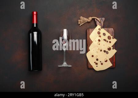 Bottiglia di vino, due bicchieri e formaggio maasdam tagliato su un tagliere su fondo arrugginito. Vista dall'alto. Foto Stock