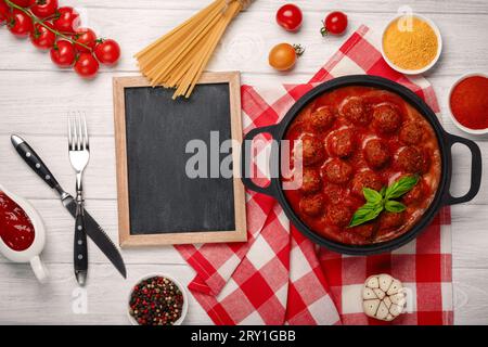 Polpette in salsa di pomodoro con spezie in padella e pomodori ciliegini su una tavola di legno bianca. Vista dall'alto con spazio per il testo. Foto Stock