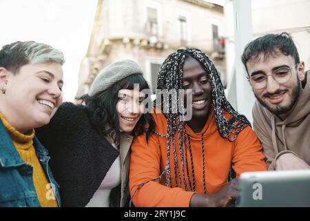 Un gruppo eterogeneo di giovani adulti, tra cui un individuo non binario con piercing colorati di capelli e naso, si riunisce all'aperto, ridendo e coinvolgendo Foto Stock