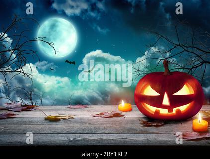 Le spaventose zucche di Halloween, Jack o Lantern, con un volto malvagio e occhi su un tavolo di legno con uno sfondo nebbioso e luna piena. Halloween Pumpkin con Foto Stock