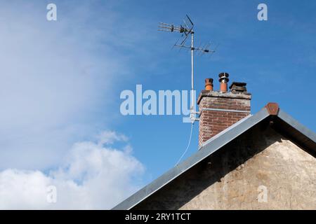 Antenna televisiva fissata al camino in mattoni sul tetto di una casa con parete di pietra calcarea. Cielo blu con nuvole. Copia spazio Foto Stock