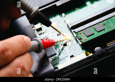 L'elettricista controlla la scheda elettronica con la sonda del multimetro digitale. Il tecnico controlla e diagnostica i problemi relativi alle schede madri del computer. Appli Foto Stock
