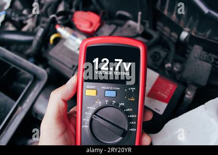 Test della tensione della batteria del veicolo con un multimetro digitale da parte di un tecnico automatico, visualizzazione della corrente di tensione del veicolo su schermo nero del multimetro digitale, manutenzione del veicolo Foto Stock