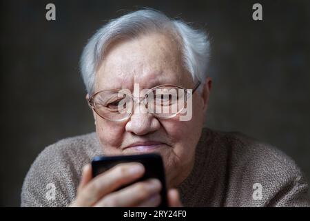 Nonna con gli occhiali che sorride guardando lo smartphone, primo piano Foto Stock