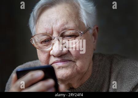 Nonna con gli occhiali che sorride guardando lo smartphone, primo piano Foto Stock