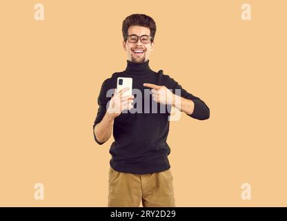 Ritratto di un giovane allegro che punta il dito verso il telefono cellulare Foto Stock