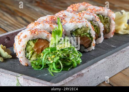 Primo piano del set servito di involtini di sushi all'uramaki al tonno con avocado e insalata di wakame su un piatto di cemento Foto Stock