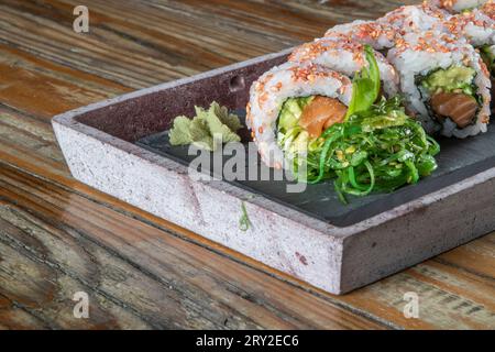Primo piano del set servito di involtini di sushi all'uramaki al tonno con avocado e insalata di wakame su un piatto di cemento Foto Stock