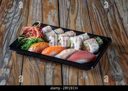 Contenitore in plastica nera da portare con set di involtini sushi al tonno uramaki e sushi nigiri con pesce assortito e insalata di alghe Foto Stock