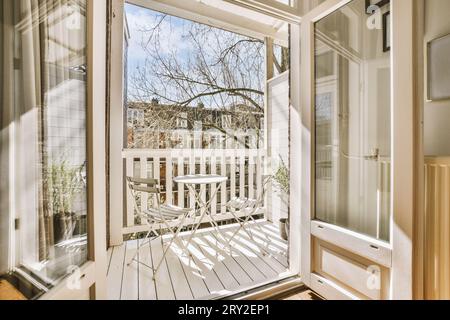 Balcone bianco con sedie vuote e tavolo disposti tramite ringhiere, visto attraverso la finestra aperta della casa moderna Foto Stock