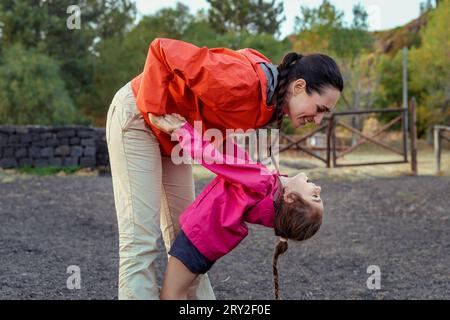 In un ambiente all'aperto, forse un parco o un agriturismo, una madre tiene la mano della figlia di tre anni, i loro occhi chiusi in uno sguardo amorevole, catturati Foto Stock
