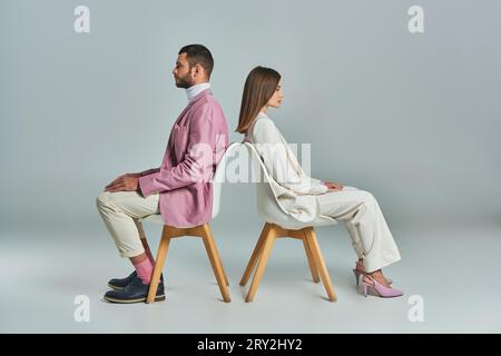 coppia moderna in abbigliamento business seduti da una parte all'altra in poltrone di stile grigio minimalista Foto Stock