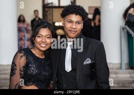 In un primo piano al ballo, una coppia mista vestita con eleganti abiti neri e formali condivide un sorriso autentico, trasudando eleganza e felicità Foto Stock