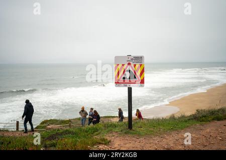 Segnale di pericolo che avverte delle grandi onde marine a Nazare, Portogallo Autumn Blured People sullo sfondo Foto Stock