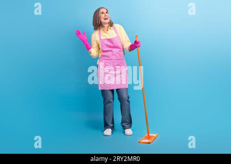 Foto a grandezza naturale di un'allegra e stravagante signora che tiene il pavimento di lavaggio dei mop sembra vuoto isolato su sfondo di colore blu Foto Stock