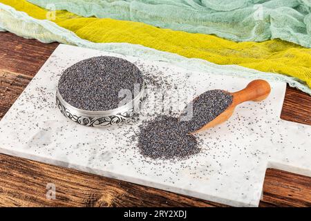 Semi di papavero. Piatto di semi di papavero con lanugine scura in mestolo di legno o cucchiaio isolato su fondo di marmo. Snack vitaminico colazione, dieta e alimentazione sana Foto Stock