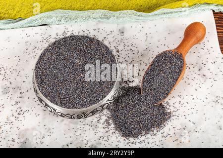 Semi di papavero. Piatto di semi di papavero con lanugine scura in mestolo di legno o cucchiaio isolato su fondo di marmo. Snack vitaminico colazione, dieta e alimentazione sana Foto Stock