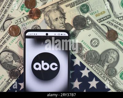 In questa immagine fotografica, il logo dell'American Broadcasting Company è visibile su uno smartphone con banconote e monete in dollari americani sul retro Foto Stock