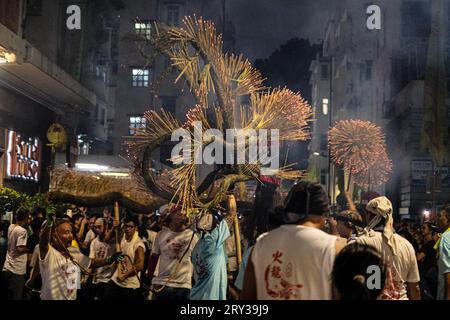 Hong Kong, Cina. 28 settembre 2023. I partecipanti a Tai Hang portano un drago e una palla drago marciano attraverso una strada. Nel XIX secolo la gente del villaggio di Tai Hang a Hong Kong credeva di aver miracolosamente fermato una peste con una danza del drago del fuoco. Da allora, è diventata una tradizione annuale, dove fino a 300 artisti ballano la danza del drago di fuoco, composta da 72.000 bastoni di incenso bruciato e un drago lungo 67 metri, attraverso le strette strade di Tai Hang. Lo spettacolo attira una folla enorme anno dopo anno ed è tornato in piena forza dopo aver diminuito la partecipazione durante il Covid Foto Stock