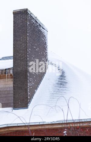 Un tetto di una casa piena di neve bianca, ad eccezione di un sentiero che si è sciolto a causa di un cattivo isolamento. C'è un grande camino in mattoni e il tetto è coperto Foto Stock