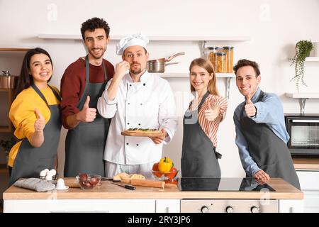 Italian chef with prepared pizza and group of young people after cooking class in kitchen Stock Photo