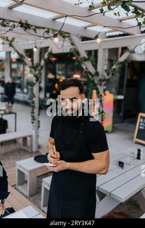 Sorridente giovane cameriere maschio che prende il cibo al ristorante Foto Stock