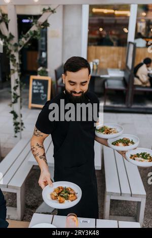 Un giovane cameriere maschio sorridente che serve cibo al ristorante Foto Stock