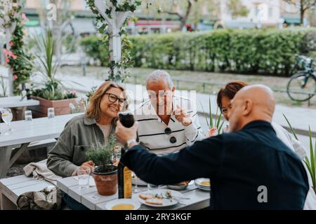 Uomo anziano che mostra smartphone ad amici maschi e femmine seduti al ristorante Foto Stock