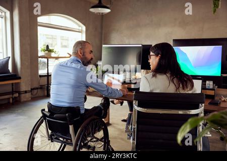 Colleghi di lavoro discutendo mentre è seduto alla scrivania in ufficio Foto Stock
