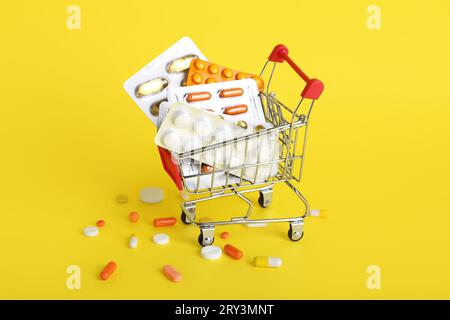 Mini carrello con diversi farmaci su sfondo giallo Foto Stock