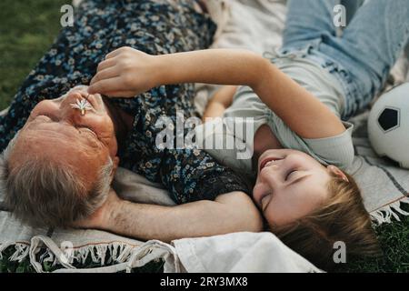 Ragazza sorridente che tiene il fiore sulla faccia del nonno mentre si stende insieme Foto Stock