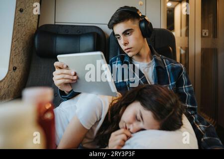 Ragazzo che guarda un tablet PC con la sorella che dorme sul grembo in treno Foto Stock